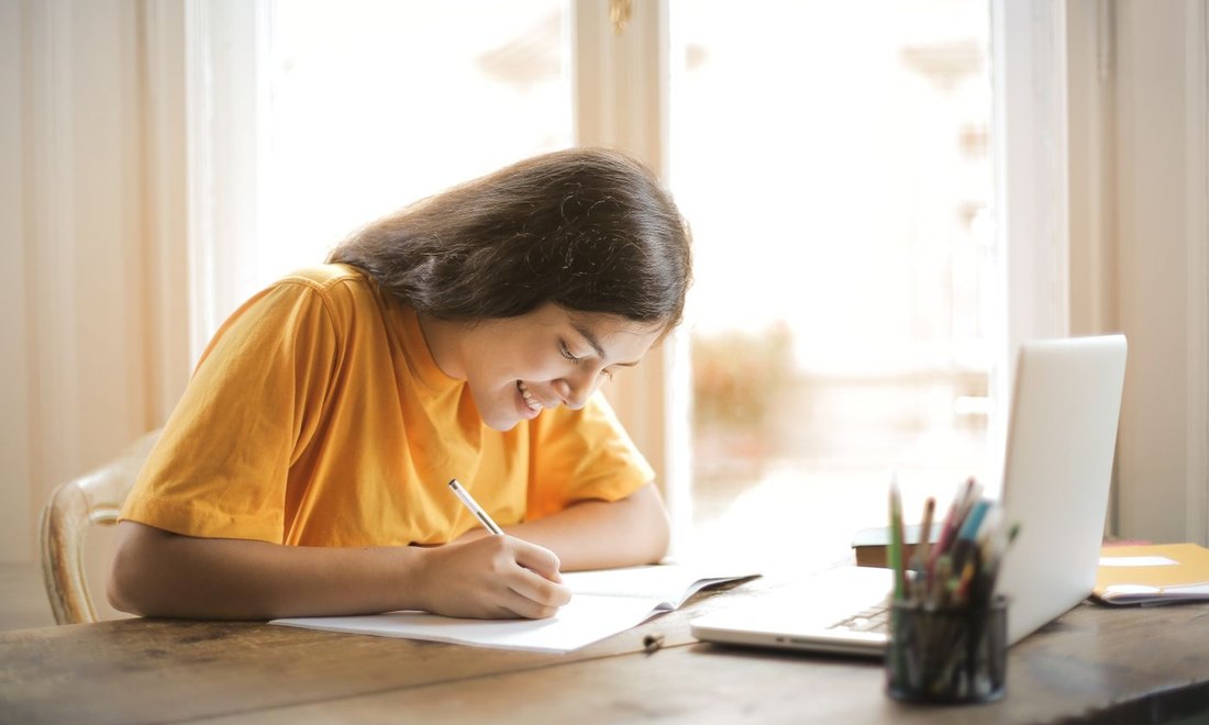 A student writing at a desk while reviewing papers